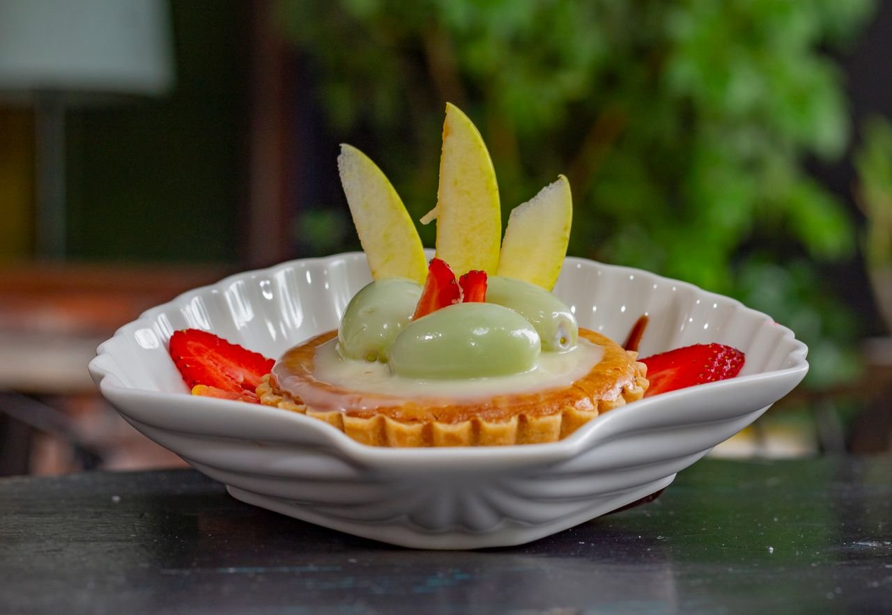 A delectable fruit tart garnished with strawberries, apple slices, and mint mousse in a white dish.