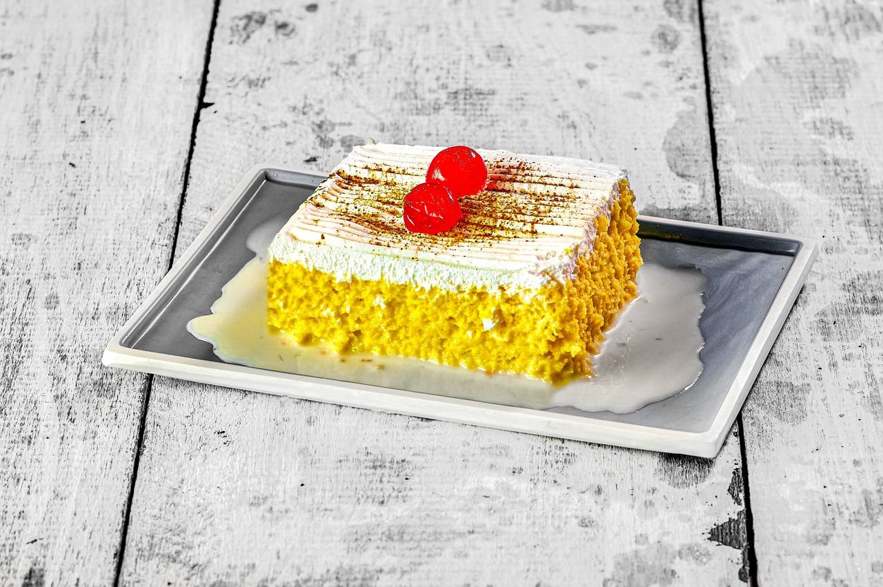 A vibrant slice of Tres Leches cake topped with cherries, captured in Quito, Ecuador.